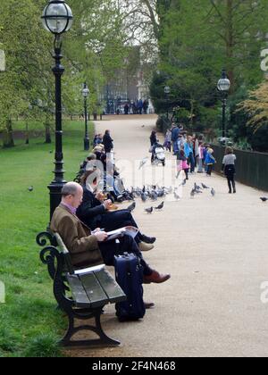 Persone che camminano e si sedevano sulle panchine in un parco londinese al sole di primavera Foto Stock
