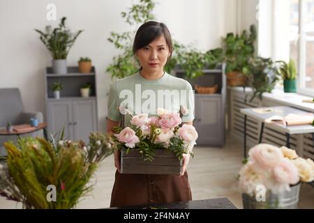 Vita in su ritratto di giovane donna asiatica che tiene i fiori e guardando la macchina fotografica mentre posa in officina fioristi, copy spazio Foto Stock