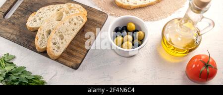 Striscione con pane affettato su tavola servito con olive, pomodori, olio d'oliva ed erbe fresche su tavola bianca con posto per il testo. Fresco, gustoso Foto Stock