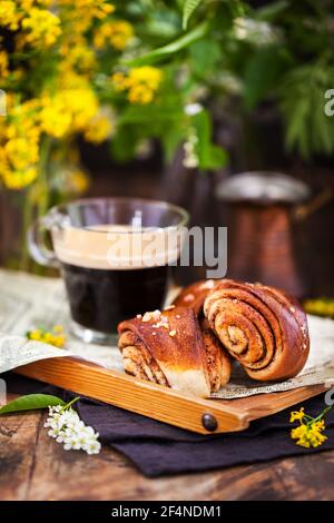 Dolci fatti in casa alla cannella e cardamomo (panini) e una tazza di caffè nero Foto Stock