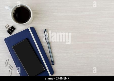 Si prega di prenotare con penna, smartphone, tazza da caffè e graffette su scrivania in legno con spazio per il testo. Vista dall'alto. Foto Stock