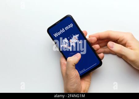 La persona tiene in mano uno smartphone con una mappa del mondo con ricerca. Foto Stock