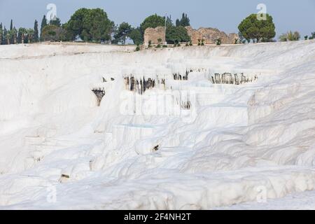 Ciotole d'acqua, travertini, pareti bianche della montagna di Pamukkale in Turchia con un antico muro in mattoni rovinato sulla parte superiore. Foto Stock