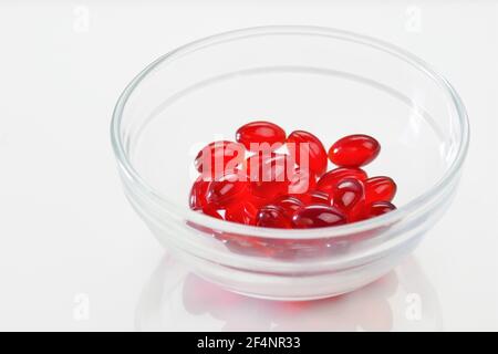 Capsule di olio di krill. Capsule di gelatina rossa con olio di krill in una tazza trasparente su fondo bianco.Fonte di acidi grassi omega.supplemento dietetico Foto Stock