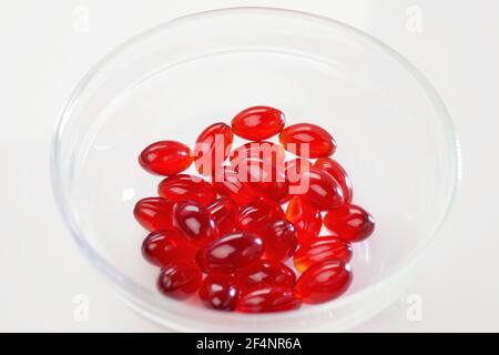 Olio di krill. Capsule di gelatina rossa con olio di krill in una tazza trasparente di vetro su sfondo bianco.Fonte di acidi grassi omega.supplemento dietetico Foto Stock