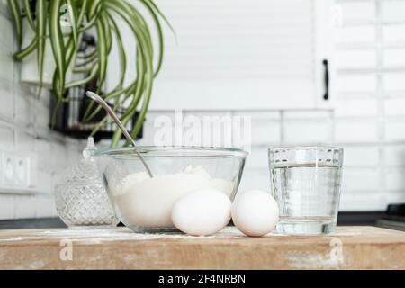 uova, farina e acqua. Fare l'impasto con le mani femminili in cucina bianca moden. Uova Foto Stock