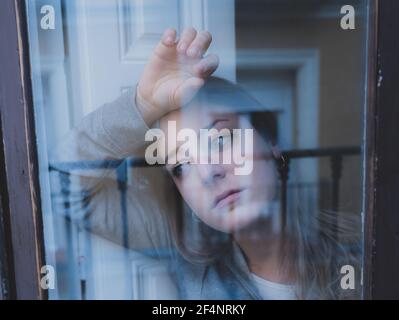 Giovane bella depressa infelice donna caucasica che guarda preoccupata e triste attraverso la finestra a casa. Sensazione di non utilità e dolore. Closeup. Depressi Foto Stock