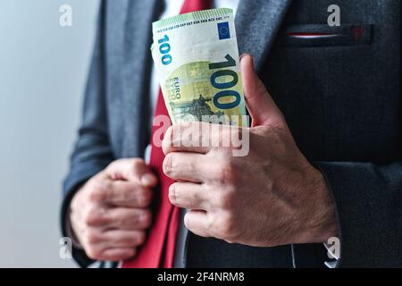 Uomo d'affari che mostra con soldi, imprenditore swagger che tiene un mazzo di cento banconote in euro in mano, fuoco selettivo Foto Stock