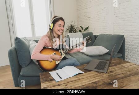 Attraente musicista donna che suona la chitarra elettrica durante il concerto online a casa in isolamento. Insegnante di musica che insegna strumento di gioco online usando l Foto Stock