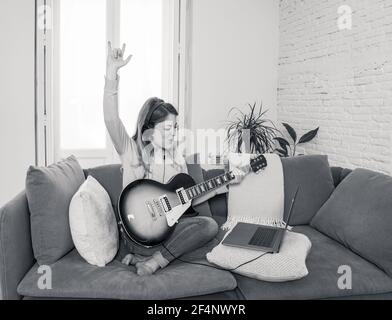 Attraente musicista donna che suona la chitarra elettrica durante il concerto online a casa in isolamento. Insegnante di musica che insegna strumento di gioco online usando l Foto Stock