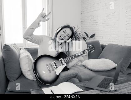 Attraente musicista donna che suona la chitarra elettrica durante il concerto online a casa in isolamento. Insegnante di musica che insegna strumento di gioco online usando l Foto Stock