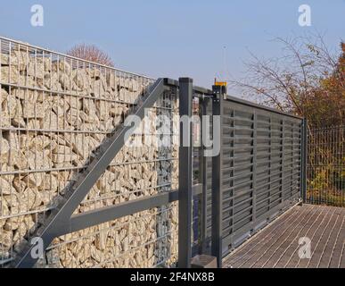 Cancello d'ingresso automatico utilizzato in combinazione con una parete di gabione. Foto Stock