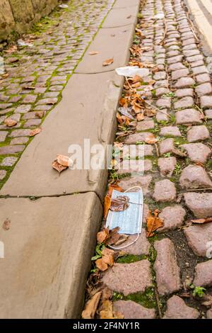 La maschera medica umida caduto sulla strada, rifiuti pandemici insostenibili lasciati dal marciapiede. La copertura del viso sporca è messa a terra a Oxford Foto Stock