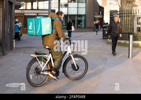 Deliveroo uomo sulla sua bici del corriere sul relativo senso a. Cliente da asporto Londra Greenwich Inghilterra Foto Stock