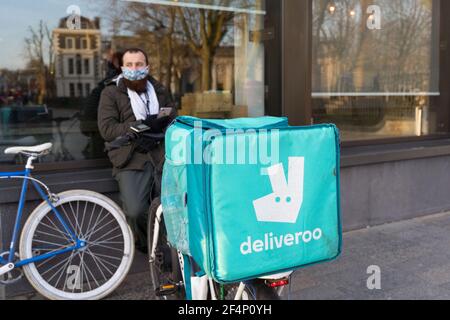 Deliveroo biker attende fuori ristorante per il suo ordine accanto alla sua moto dotata di borsa posteriore, Londra , Inghilterra Foto Stock