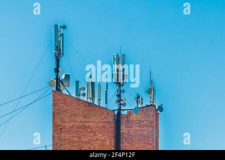 Torre di mattoni per telecomunicazioni con antenne wireless mobili su sfondo blu. Foto Stock