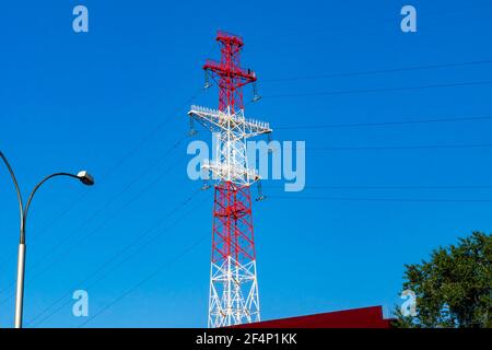 la torre a traliccio ad alta tensione dipinta in bianco e rosso, con lampade di segnalazione per l'illuminazione di emergenza e pannelli solari, si trova in città sulle rive del Foto Stock