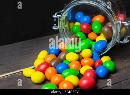 Colorate palle di cioccolato in vaso di vetro caduto in legno vintage sfondo. Foto Stock