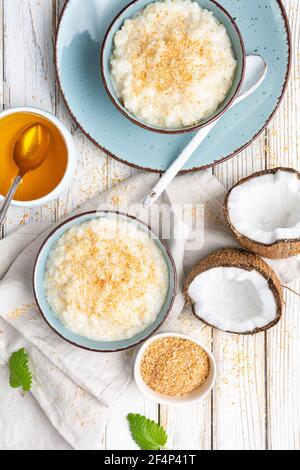 Dolce e cremoso budino di riso al cocco con miele, condito con cocco grattugiato e tostato in una ciotola in ceramica Foto Stock