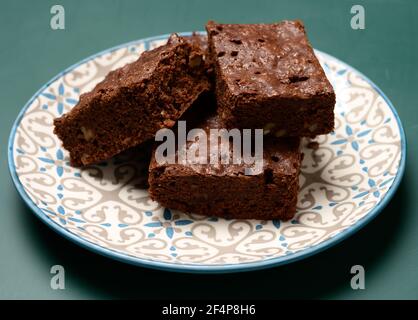 pezzi quadrati al forno di torta al cioccolato di noce brownie giacciono in un piatto rotondo, primo piano Foto Stock