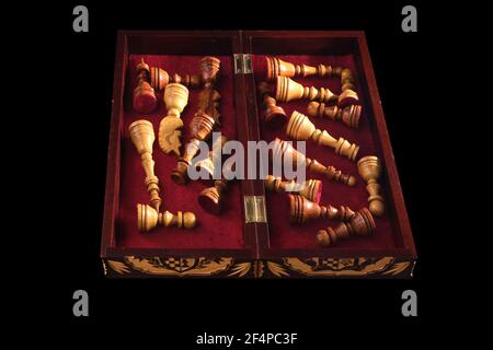 Pezzi di scacchi scolpiti sono messi via in una scatola di legno con stoffa rossa. Pezzi di scacchi fatti a mano su sfondo nero Foto Stock