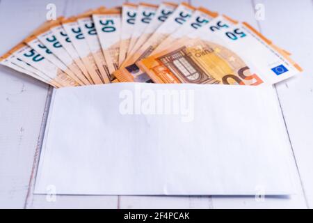 Primo piano di 50 euro di bollette in una busta sopra una superficie di legno Foto Stock