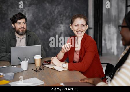 Ritratto di giovane donna d'affari sorridente che indossa giacca rossa durante l'incontro con i colleghi in ufficio, copy space Foto Stock