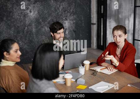Vista ad alto angolo in diversi gruppi di uomini d'affari che si riuniscono al tavolo, concentrarsi sulla giovane donna d'affari che indossa una giacca rossa e condividere idee Foto Stock