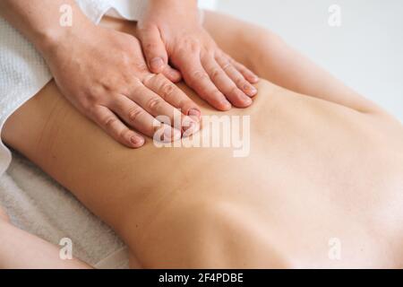 Vista dall'alto del massaggiatore maschile che massaggia la parte posteriore di una giovane donna irriconoscibile sdraiata sul tavolo da massaggio. Foto Stock