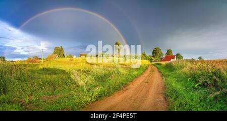 Arcobaleno sopra il cielo tempestoso. Paesaggio rurale con arcobaleno su cielo scuro tempestoso in campagna in estate sera. Foto Stock