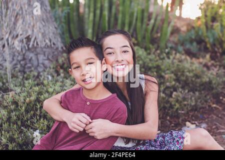 Sorella maggiore abbracciando un giovane fratello da un giardino di cactus Foto Stock