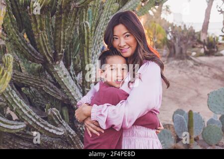 Madre abbracciando il figlio di fronte ad un grande cactus, entrambi guardando la macchina fotografica. Foto Stock