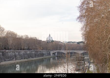 Roma. Italia. Primavera 2020. Argini romani primaverili. La gente cammina lungo l'argine. I rami di platani si piegano sul fiume Tevere. La cupola Foto Stock