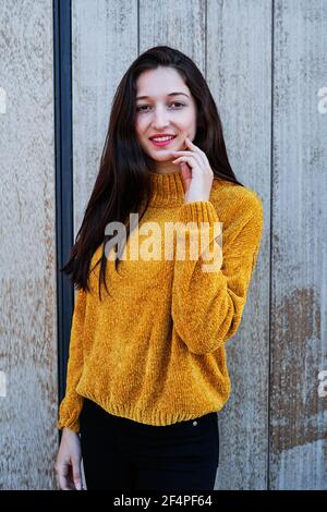 Foto verticale di un Ritratto di una giovane bruna con labbra dipinte e in un maglione giallo su a. sfondo di legno Foto Stock