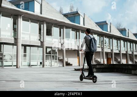Giovane uomo che guida un veicolo elettrico scooter fuori dall'edificio moderno Foto Stock