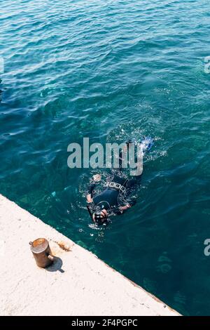 Un subacqueo in un costume da immersione con pesi, pinne e una maschera con uno snorkeling galleggia sulla superficie dell'acqua, vista dall'alto. Foto Stock