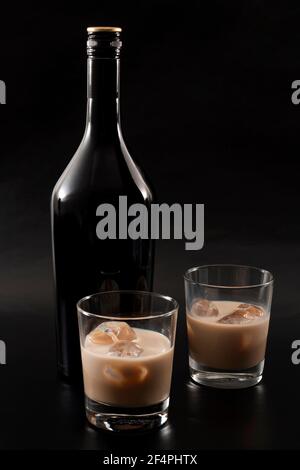 Liquore al caffè e bevande alcoliche a base di latte e whisky Concetto con bottiglia di gelato irlandese e bicchieri con ghiaccio isolato su sfondo nero scuro Foto Stock