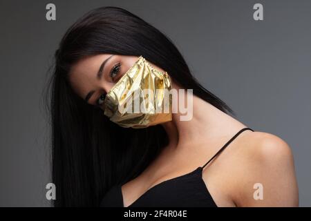 aumento di prezzo di maschere facciali e scarsità in COVID-19 volte concetto come una bella giovane donna che indossa una maschera facciale in oro perché può permetterselo Foto Stock