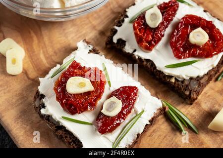 Sandwich fatti in casa con pane multigrain con formaggio cremoso e pomodori secchi su un piatto di legno, primo piano. Concetto di cibo sano Foto Stock