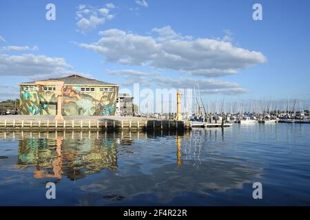 Riflesso d'acqua delle barche a vela e costruzione con murale sulla parete in una giornata nuvolosa ma soleggiata vicino al molo di San Pete. San Pietroburgo, Florida, Stati Uniti Foto Stock