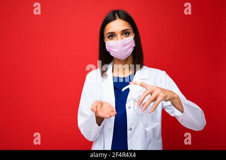 Consigli medici e protezione della salute durante l'epidemia di coronavirus. Giovane donna dottore in maschera protettiva, cappotto bianco mostra antisettico nelle sue mani Foto Stock