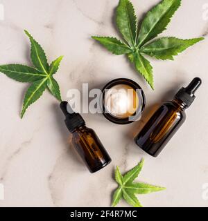 Vista dall'alto del concetto di contagocce di olio o siero con superficie di Cannabis. Cosmetica naturale. Olio CBD, tintura THC e foglie di canapa su un doppio marmo e nero backgroun Foto Stock