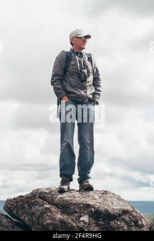 Un turista con uno zaino si erge sulla cima della montagna e ammira la vista dall'alto. Il concetto di vacanza, viaggio e vita attiva. Foto Stock