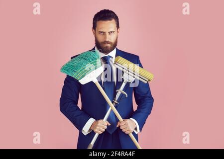 Bell'uomo d'affari con scopa per la pulizia su sfondo rosa. Uomo d'affari che pulisce vestito. Foto Stock