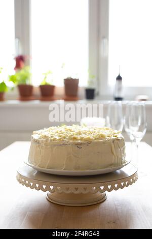Bella torta di cioccolato bianco decorata con scaglie di cioccolato bianco, su un supporto per torte. Accanto ci sono alcuni bicchieri di champagne. Foto Stock
