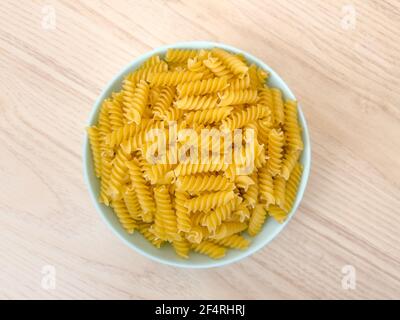 Pasta italiana secca grezza a spirale in ciotola su tavola di legno in cucina. Cibo sfondo. Vista dall'alto. Maccheroni non cotti. Foto Stock