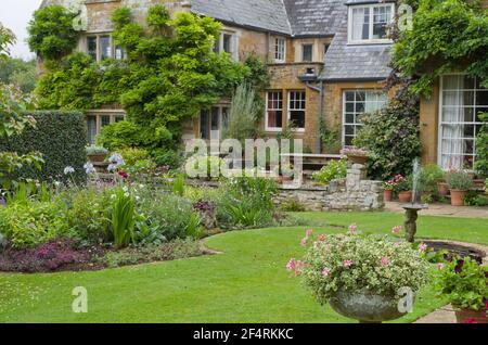 Estate a Coton Manor Gardens, Northamptonshire, Regno Unito; prato, fiori confina con il maniero del 17 ° secolo in background. Foto Stock