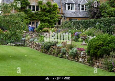 Estate a Coton Manor Gardens, Northamptonshire, Regno Unito; prato, fiori confina con il maniero del 17 ° secolo in background. Foto Stock