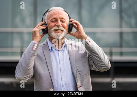 Ritratto all'aperto di un uomo d'affari anziano che sta godendo la musica sulle cuffie. Foto Stock