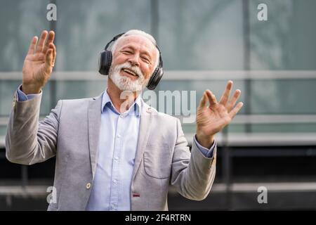 Ritratto all'aperto di un uomo d'affari anziano che sta godendo la musica sulle cuffie. Foto Stock